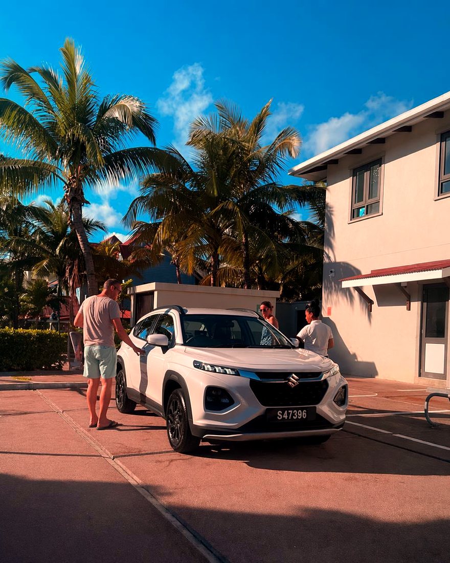 A guest collecting a white Suzuki outside a guesthouse on Mahé